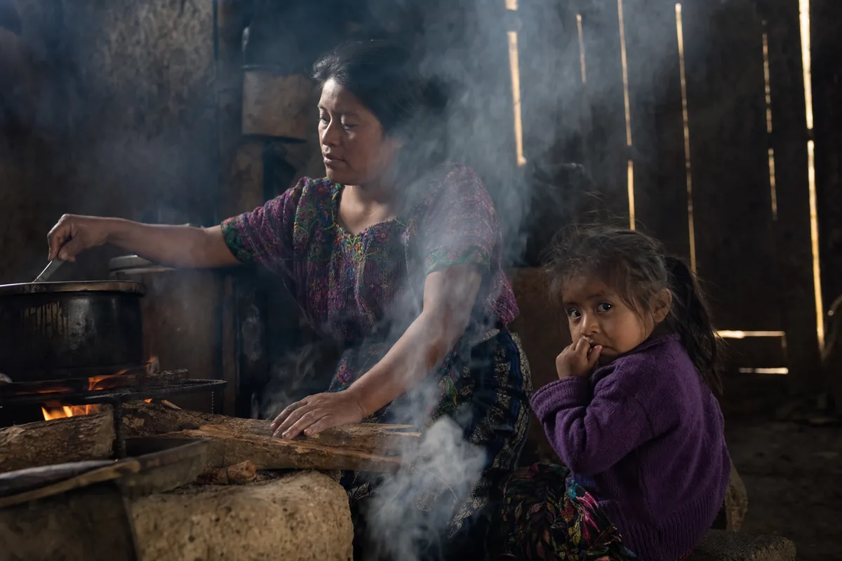 Familia rural cocinando con humo de fogón abierto dentro del hogar
